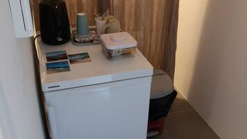 Een kleine keuken met een witte koelkast, een koffiezetapparaat, een klein spoelgedeelte en een aanrecht met enkele spullen.