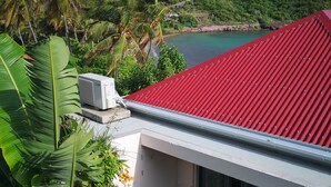Un bâtiment moderne avec un toit rouge, entouré d’une végétation luxuriante et offrant une vue sur une zone côtière.