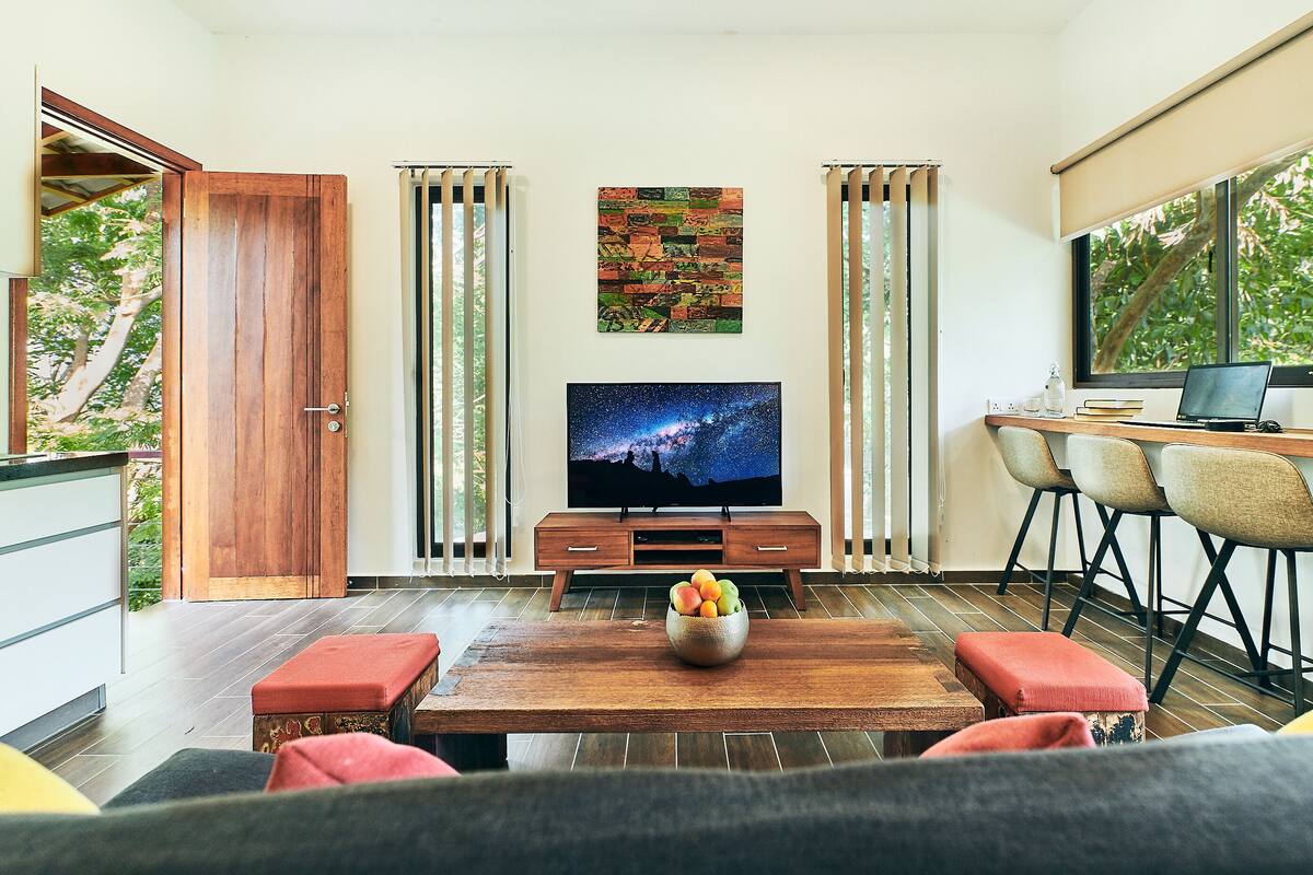 Uma sala de estar moderna com uma mesa de centro de madeira, uma TV de tela plana e uma área de jantar com cadeiras.