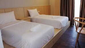Ein Hotelzimmer mit zwei Einzelbetten, Holzkopfteilen, einem Holzstuhl und einem Vorhangfenster.