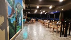 Ein Restaurant mit einer langen Theke, Holzstühlen und einem Wandgemälde eines Dinosauriers.