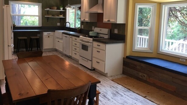 A kitchen with white cabinets, a wooden table, and a built-in bench by the windows. - Sunflower House near Skiing, boating and Apple Hill (Pollock Pines)
