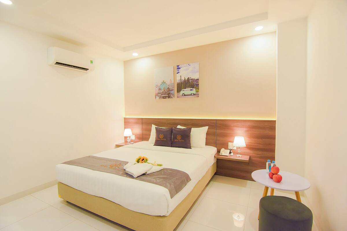 A hotel room with a bed, bedside tables, a small round table with fruit, and wall art.