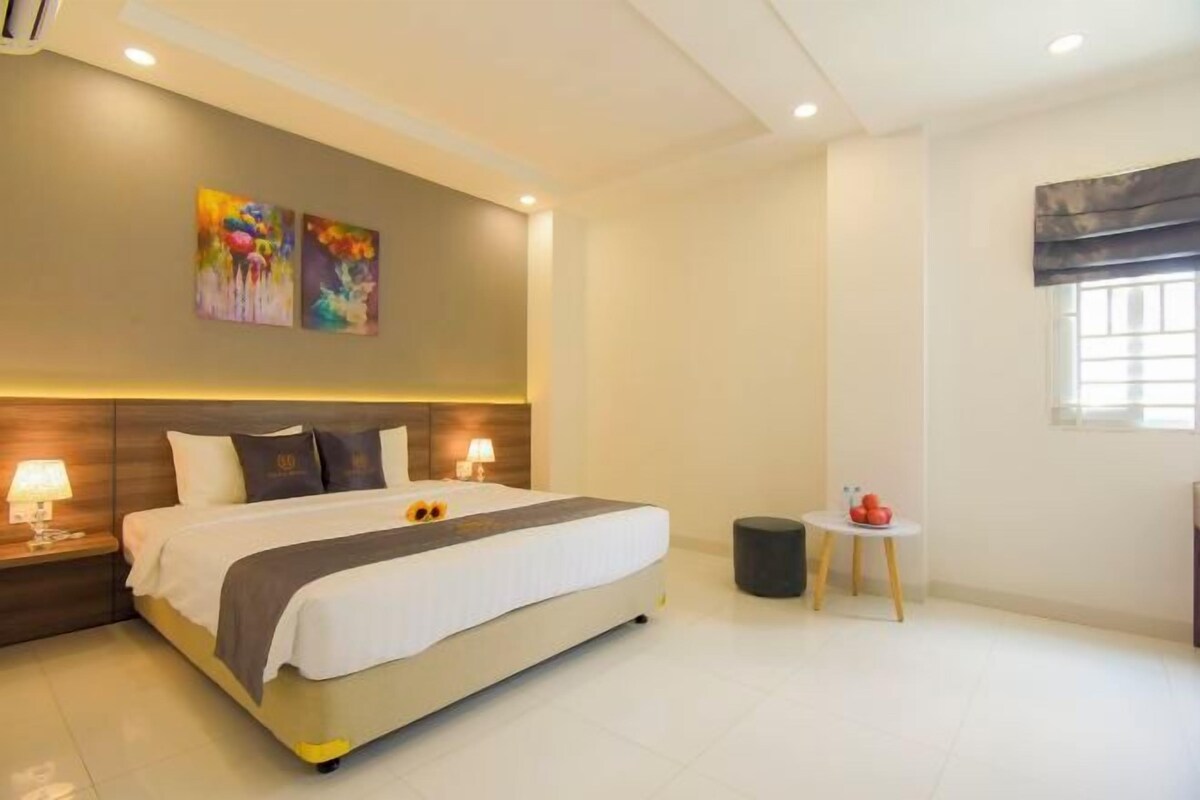 A modern hotel room with a large bed, bedside lamps, a small table with fruit, and abstract art on the wall.
