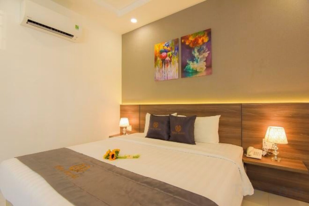 A hotel room with a bed, bedside lamps, a wall-mounted air conditioner, and two paintings.