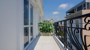 A narrow balcony with a potted plant, a black wrought iron railing, and a view of a building with a balcony in the background. - Hera Hotel (Ho Chi Minh City)