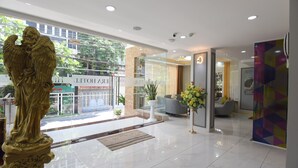 A modern hotel lobby with a statue, a reception desk, and a seating area with a sofa and armchairs. - Hera Hotel (Ho Chi Minh City)