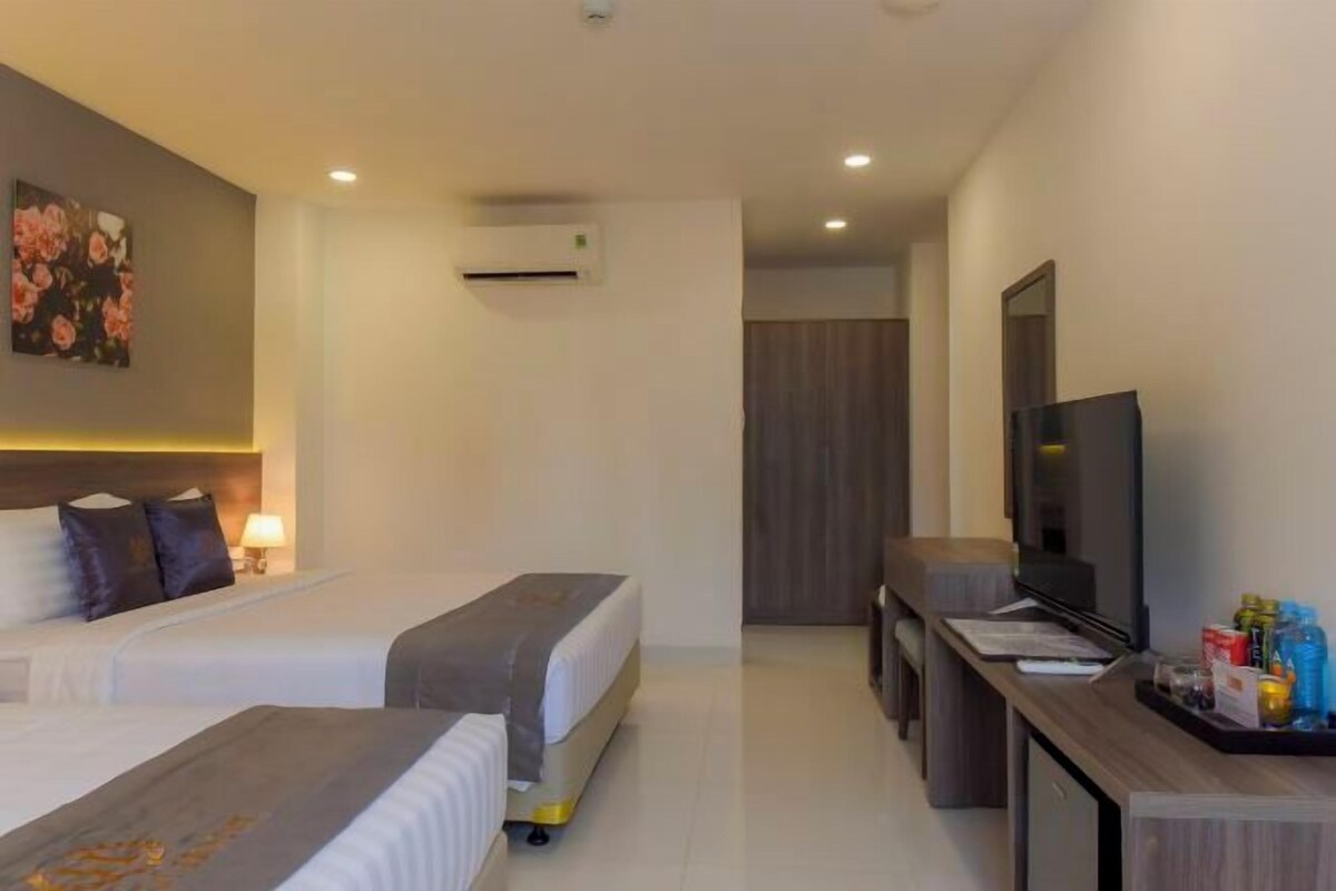 A hotel room with two beds, a desk with a flat-screen TV, and a minibar.