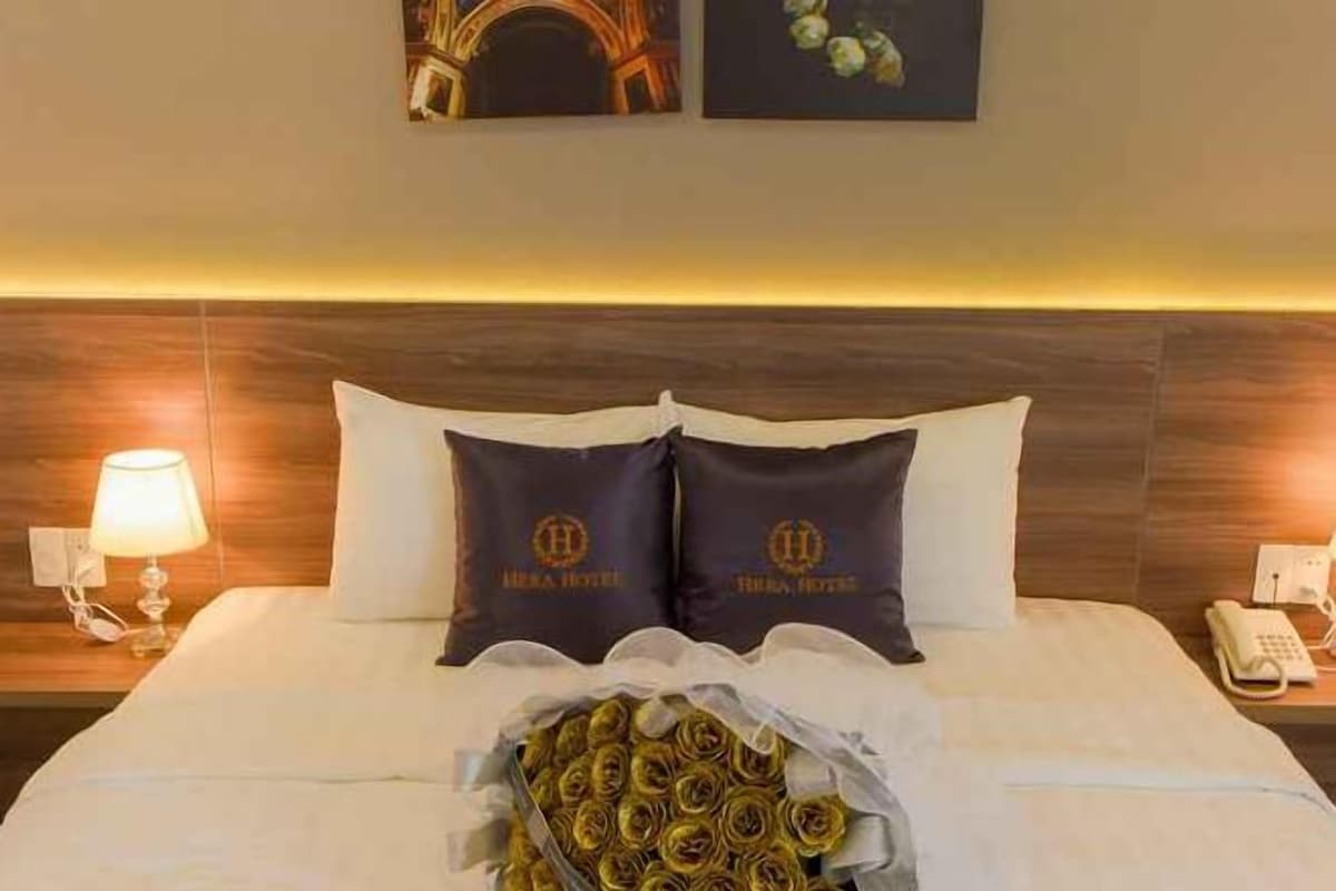 Une chambre d’hôtel avec un lit, deux oreillers portant le logo de l’hôtel, une lampe de chevet et un téléphone sur la table de chevet.