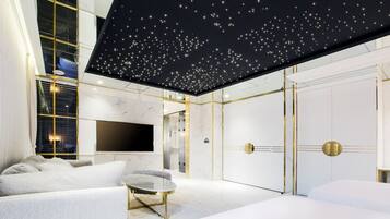 Quarto de hotel moderno com teto estrelado, uma televisão de tela plana grande, um sofá e uma cama.