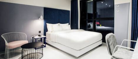 A modern hotel room with a large bed, a desk, a chair, and a round table.