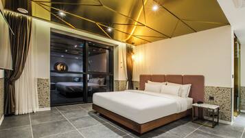 Ein modernes Hotelzimmer mit einem großen Bett, einem kleinen Beistelltisch und Blick durch eine Schiebetür auf einen Balkon.