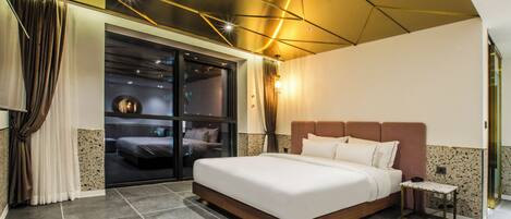 Een moderne hotelkamer met een groot bed, een klein bijzettafeltje en een uitzicht door een schuifdeur naar een balkon.