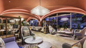 Eine moderne Lounge mit gewölbten Decken, einem zentralen Kronleuchter und Sitzbereichen mit Tischen.