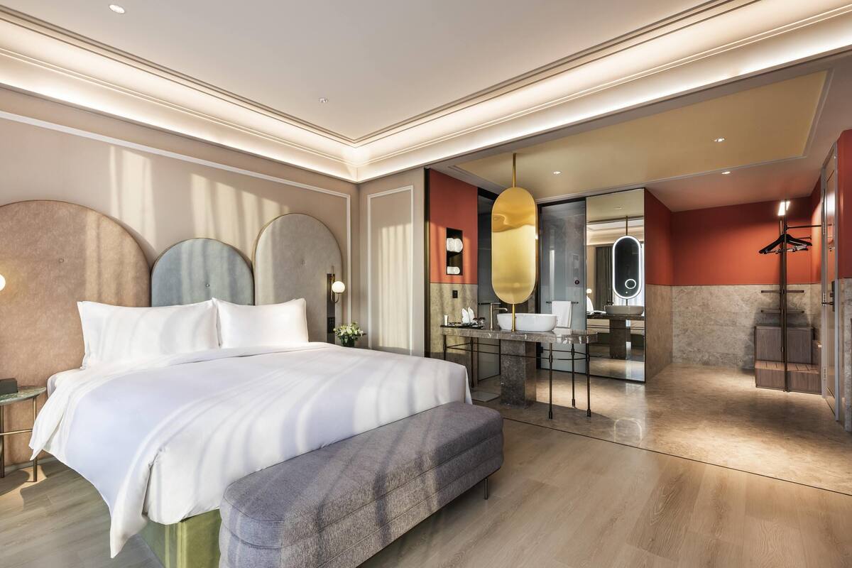 Een moderne hotelkamer met een groot bed, een bankje, een badkamer met spiegel en een douche.