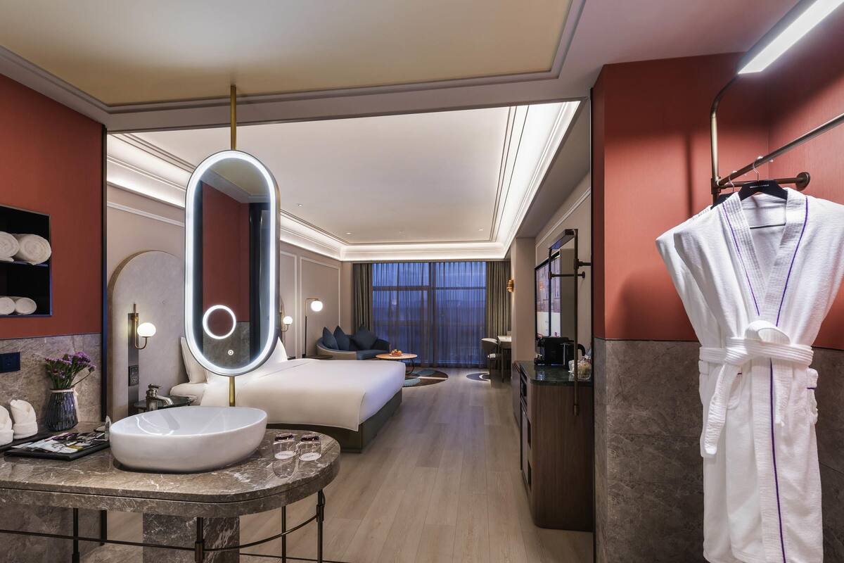 Hotelkamer met een groot bed, een rond badkamermeubel, een spiegel, een badjas en uitzicht op de stad.