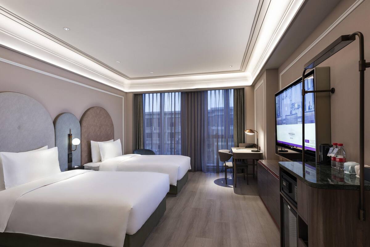 Een hotelkamer met twee bedden, een bureau, een televisie en een minibar.