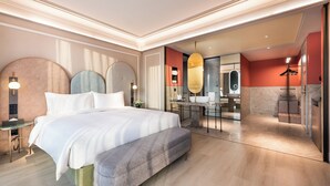 Ein modernes Hotelzimmer mit einem großen Bett, einem Schreibtisch und einem Badezimmer inklusive Spiegel und Waschbecken.