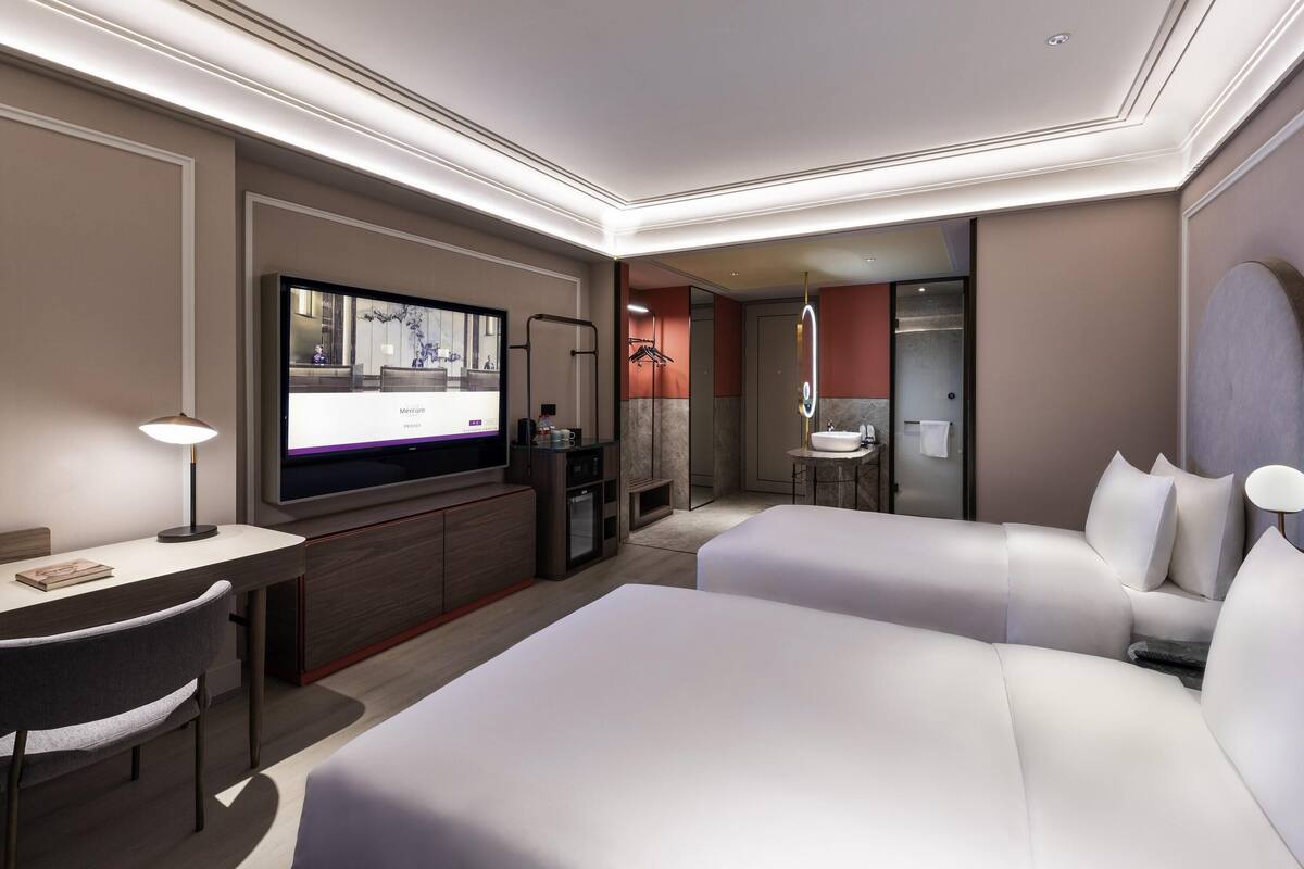 Een hotelkamer met televisie, bureau, twee bedden, badkamer en minibar.