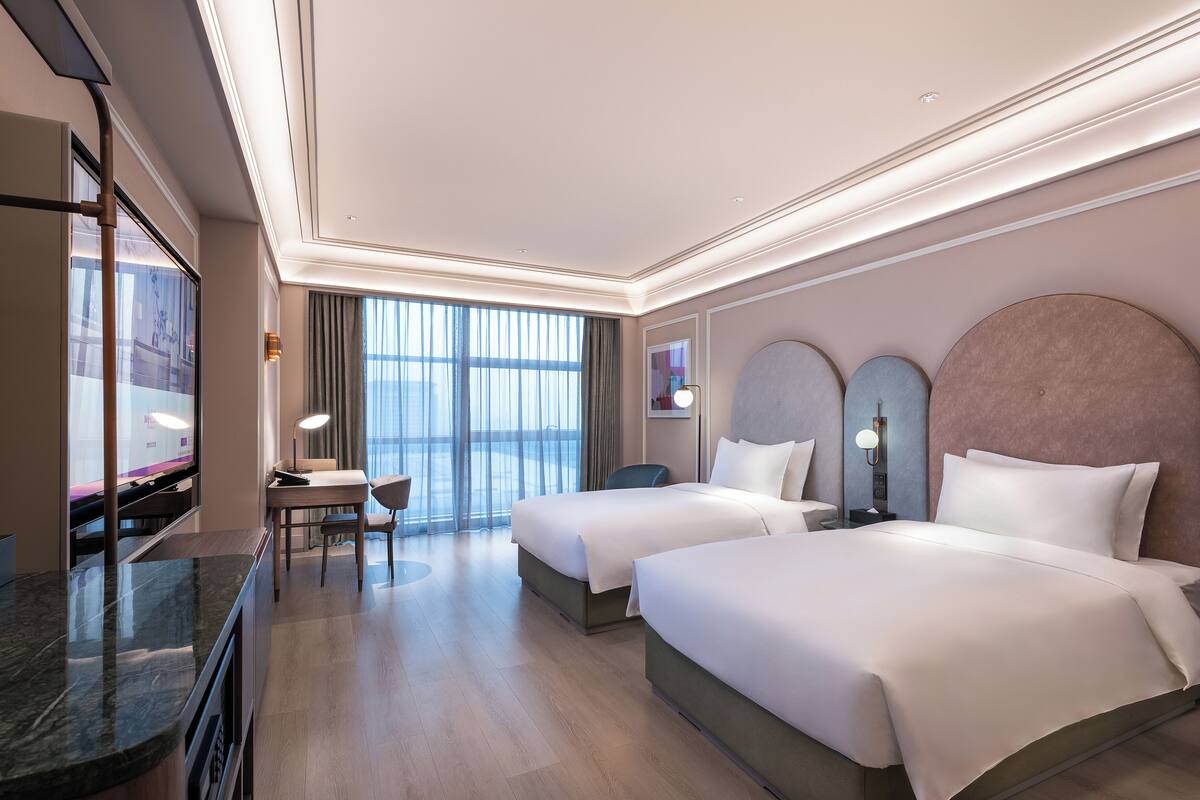 Een hotelkamer met twee bedden, een bureau, een televisie en een groot raam.