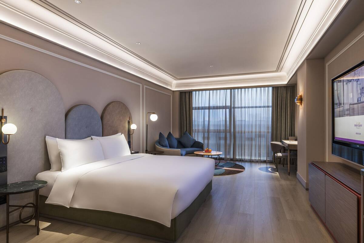 Een moderne hotelkamer met een groot bed, een zithoek met uitzicht, een bureau en een televisie.