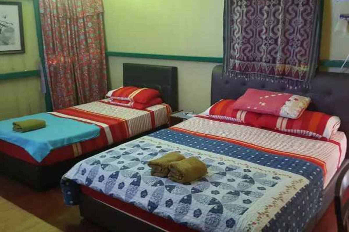 A room with two single beds, each with a red and white striped bedspread and matching pillows. There is a blue bedspread on the left bed and a patterned bedspread on the right bed. A brown bag is placed on the left bed.