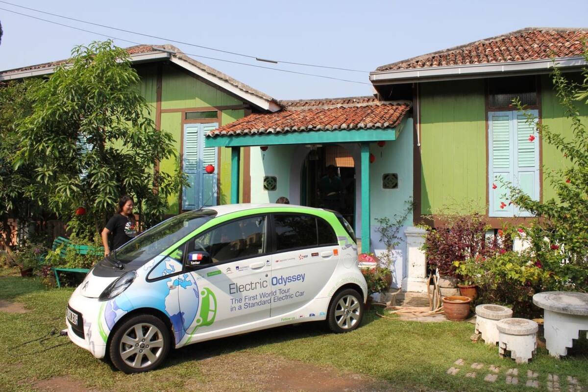 A small electric car parked in front of a house with a tiled roof and green walls.