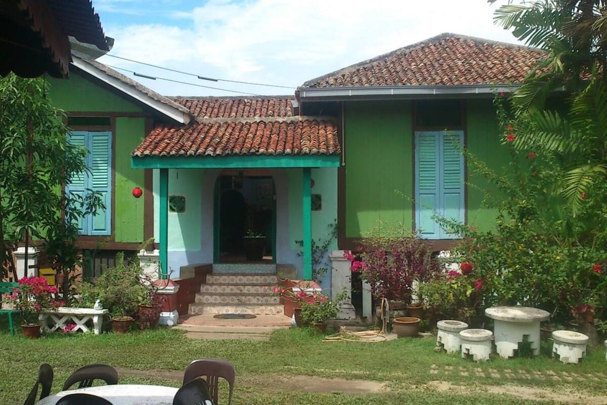 A two-story house with a tiled roof, green walls, and a front porch with steps leading to the entrance.