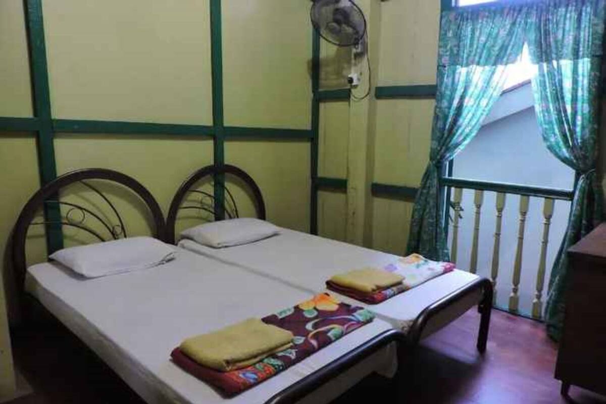 A room with two single beds, a fan, and a window with curtains.