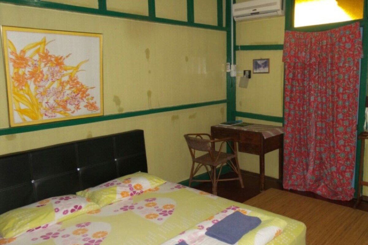 Una habitación con cama, escritorio, silla, ventana con cortina y aire acondicionado.