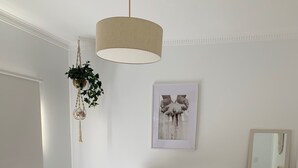 Une chambre à coucher comprenant un lit, des tables de chevet, une plante suspendue, un tableau encadré, un miroir et un tapis à motifs.
