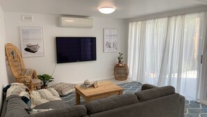 Un salon moderne avec un canapé gris, un fauteuil en osier, un téléviseur à écran plat et une petite table basse en bois.