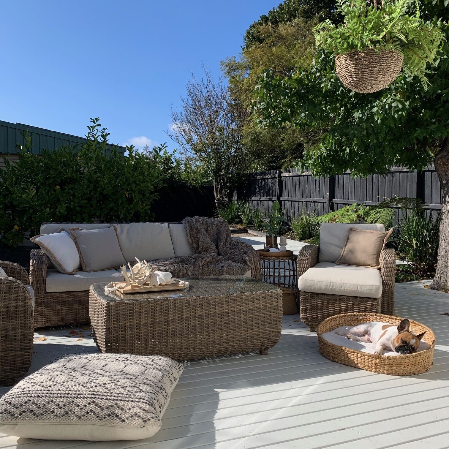 A patio with wicker furniture, including a sofa, chairs, and ottomans, and a dog bed.