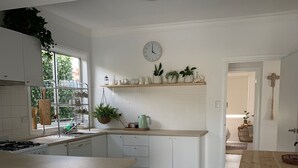 Une cuisine moderne avec des meubles blancs, un îlot central en bois doté de tabourets, une plante suspendue et une horloge au mur.