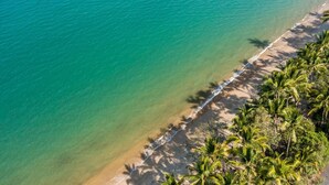 Luchtbeeld van een strand met helder turquoise water, een zandstrand en palmbomen.