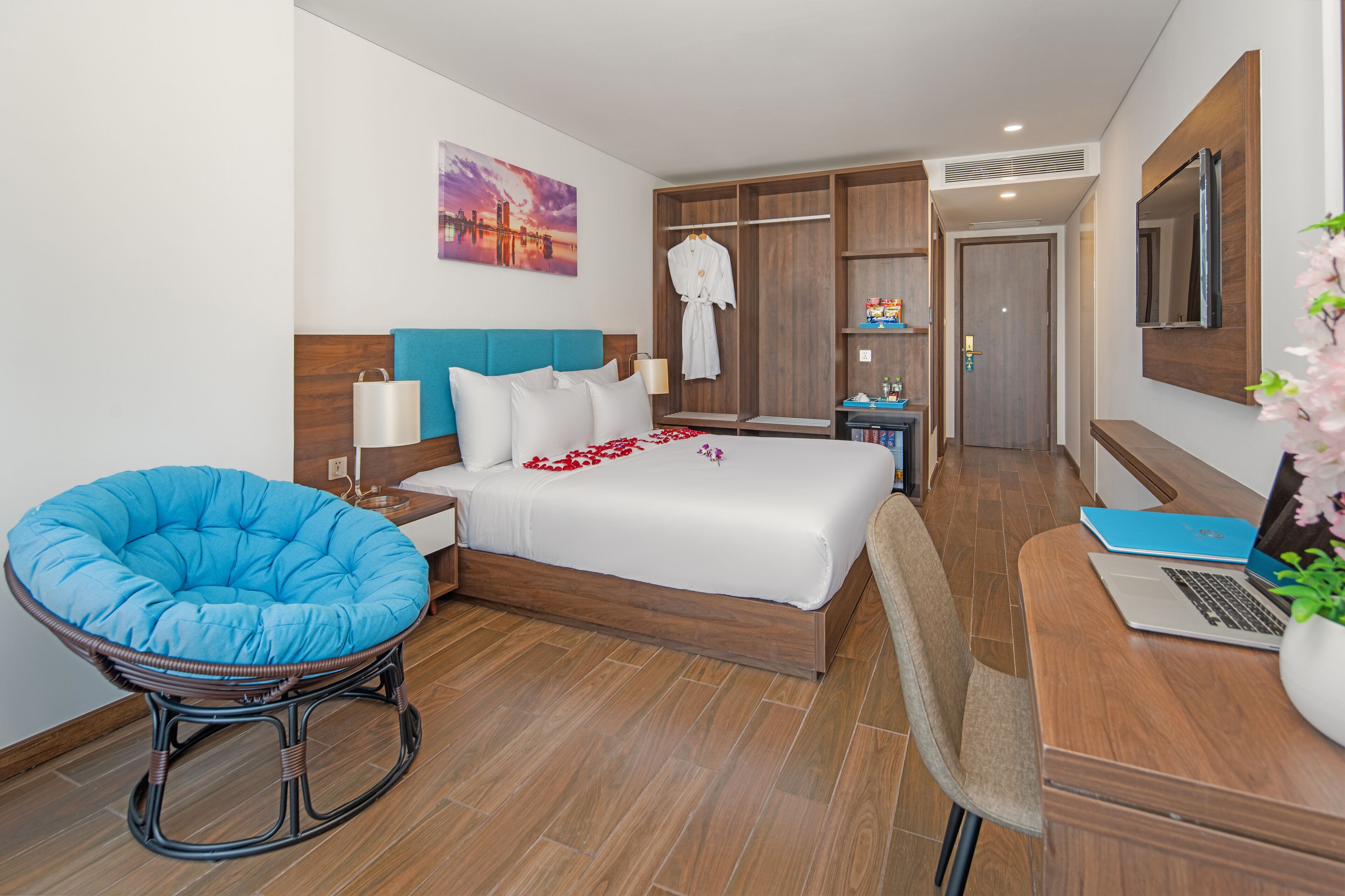 Una habitación de hotel moderna con una cama grande, una silla azul, un escritorio con una computadora portátil y un armario.