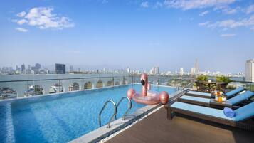 A rooftop infinity pool with a city view, lounge chairs, and a pink flamingo float.