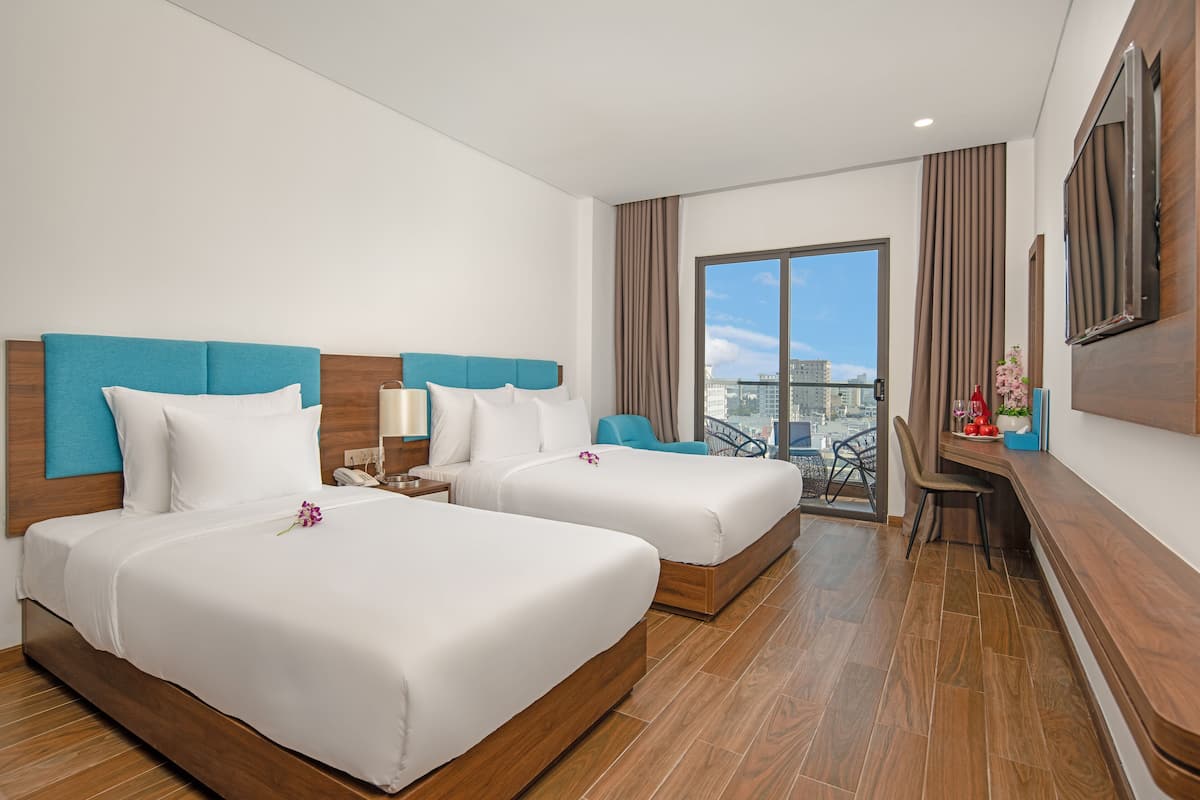 A hotel room with two beds, a desk, a chair, a TV, and a balcony with a city view.