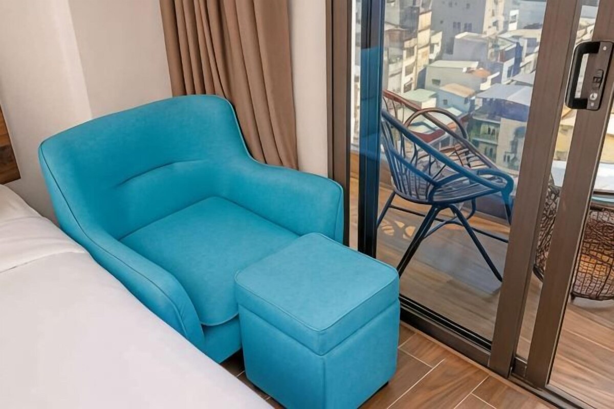 Quarto com um sofá e apoio para os pés azuis, e uma porta de vidro que dá para uma varanda com cadeiras azuis.