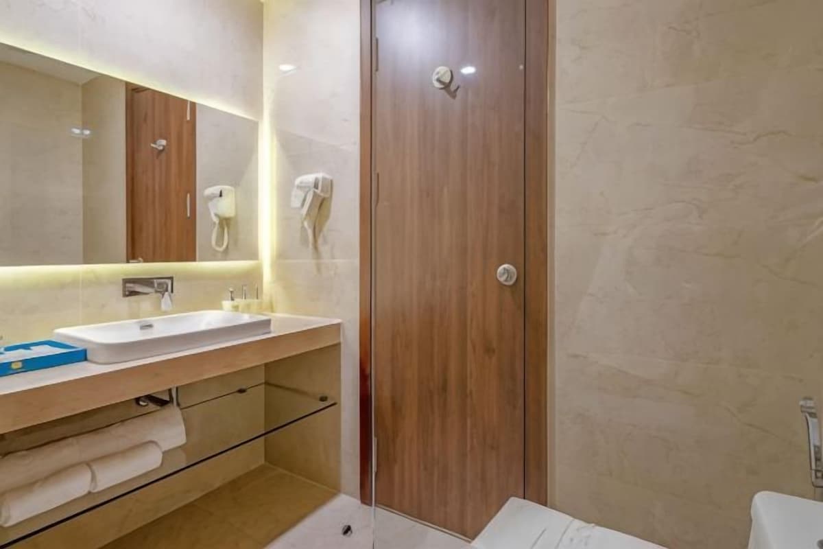 Un baño moderno con tocador de madera, un espejo grande, un lavabo blanco y un box de ducha de vidrio.