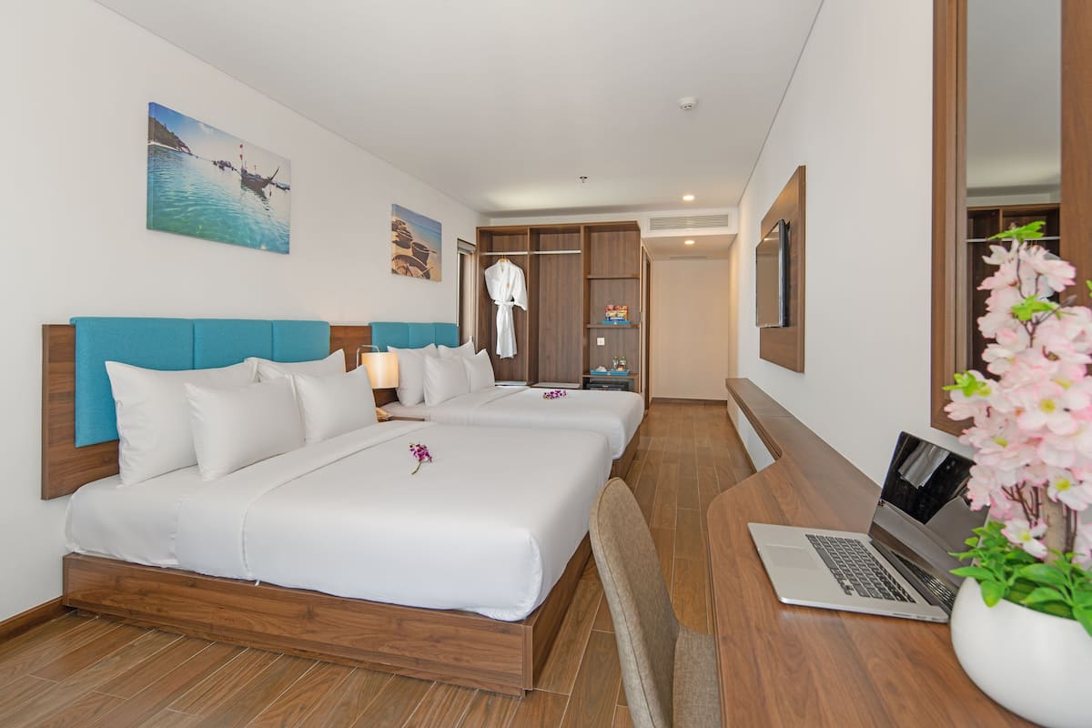 A hotel room with two beds, a laptop on a desk, a robe hanging, and a painting on the wall.