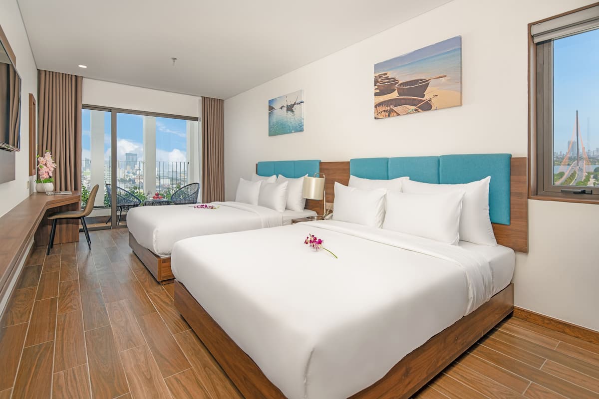 A hotel room with two beds, a desk, and a chair. There are large windows with a view of the city and a bridge.