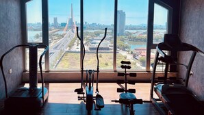 Ein Fitnessstudio mit Trainingsgeräten und großen Fenstern, die einen Blick auf die Stadt ermöglichen.