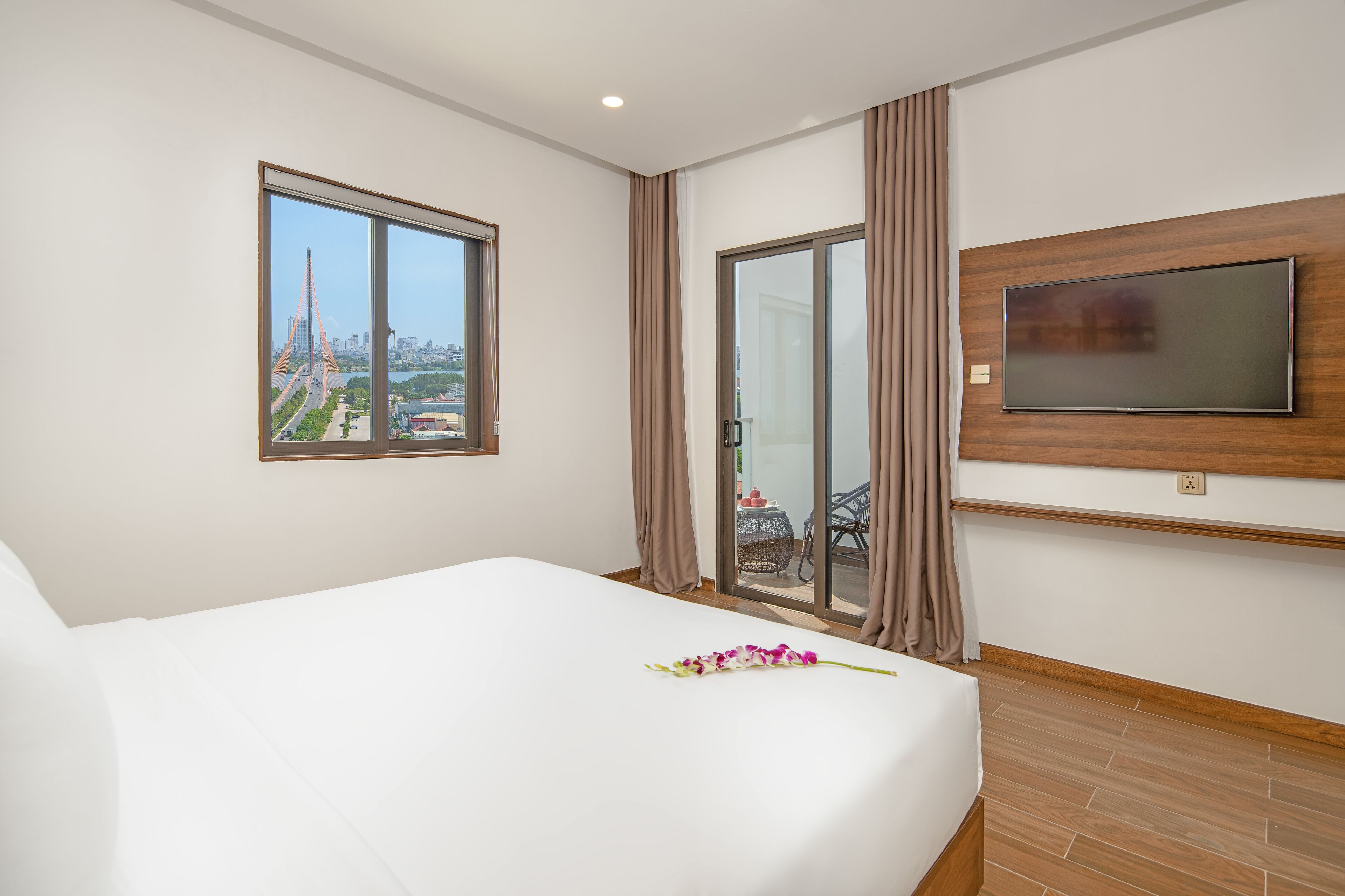 A hotel room with a large bed, a TV mounted on the wall, a window with a city view, and a sliding glass door.
