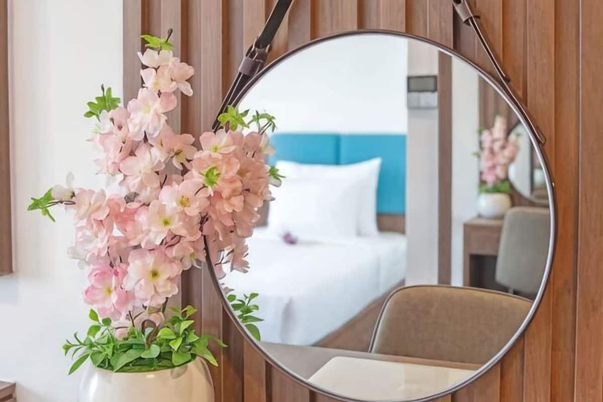 A mirror with a floral arrangement, a bed with white bedding, and a blue headboard in the background.