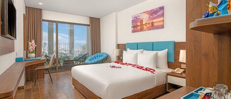 Una habitación de hotel moderna con una cama grande, un balcón con vistas, un escritorio y un televisor.