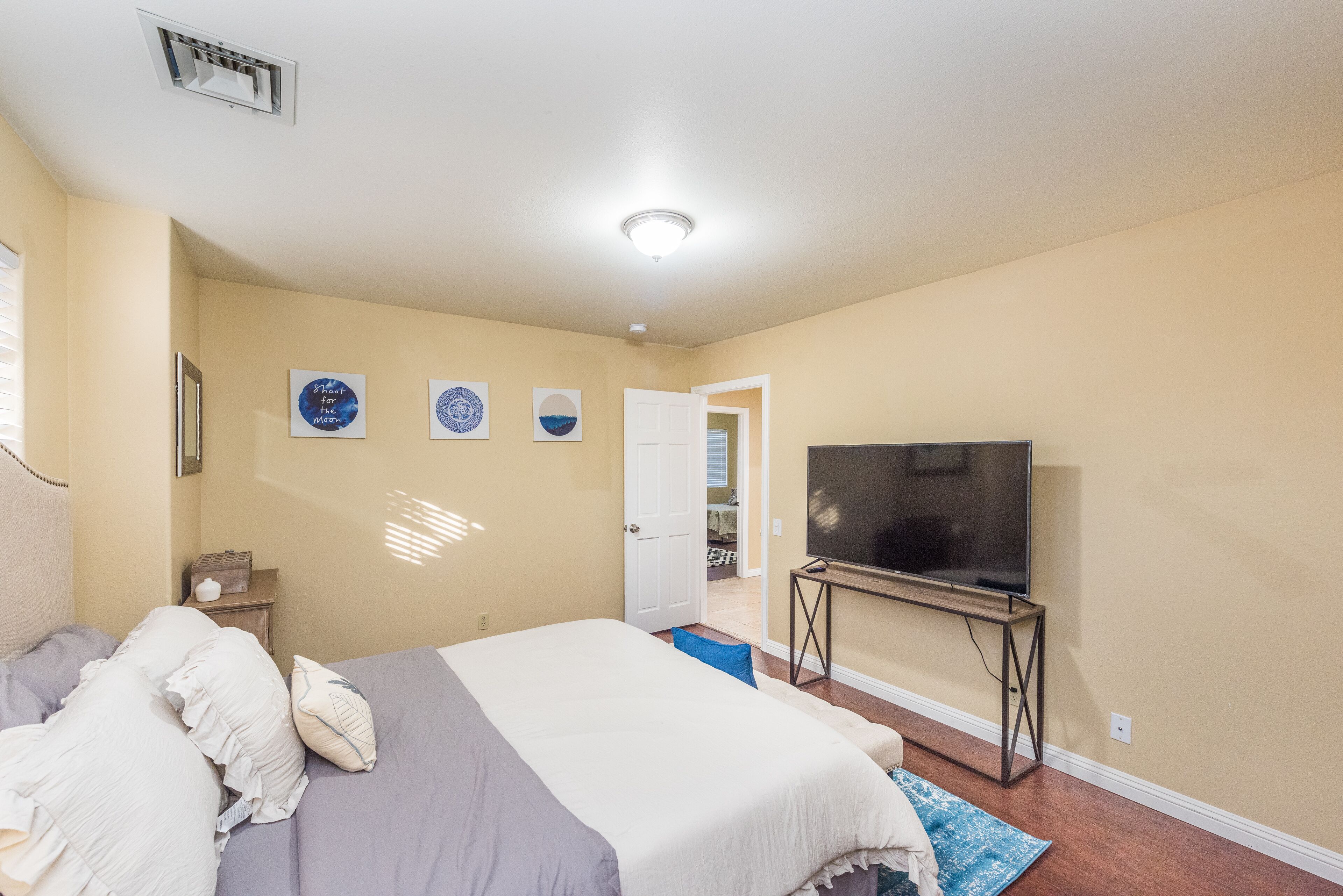 A bedroom with a bed, a TV on a stand, and a door leading to another room.
