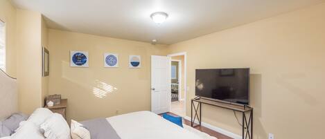 A bedroom with a bed, a TV on a stand, and a door leading to another room.