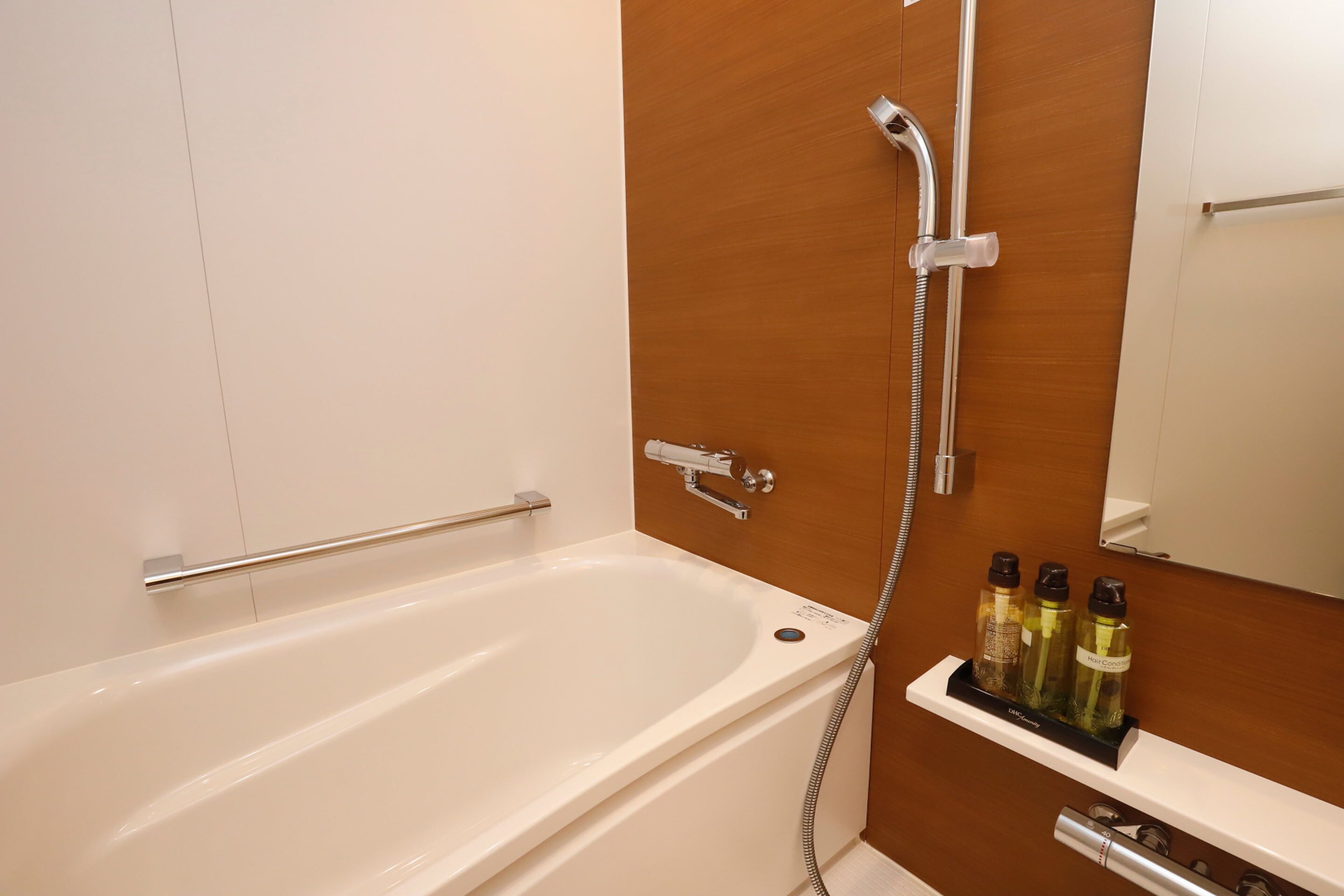Une salle de bain moderne avec une baignoire blanche, une porte en bois, une douche avec un pommeau de douche amovible et une étagère contenant des articles de toilette.
