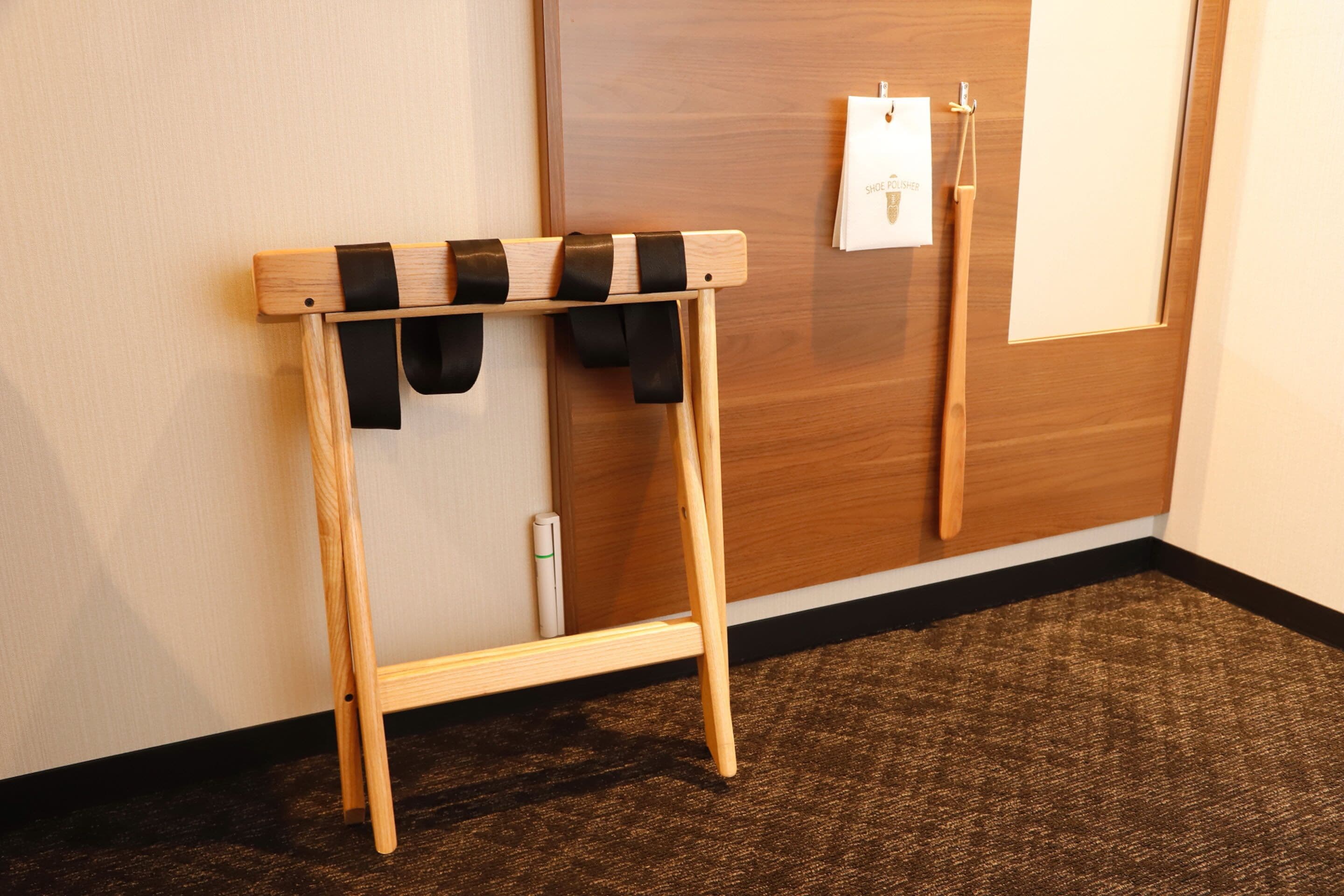 Un zapatero de madera con correas negras, frente a una puerta y pared de madera.